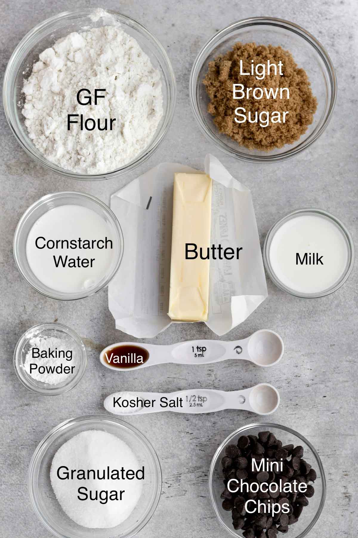 The ingredients for Chocolate chip sugar cookies which are gluten free flour, light brown sugar, cornstarch water, butter, milk, baking powder, vanilla, kosher salt, granulated sugar and mini chocolate chips in separate containers.