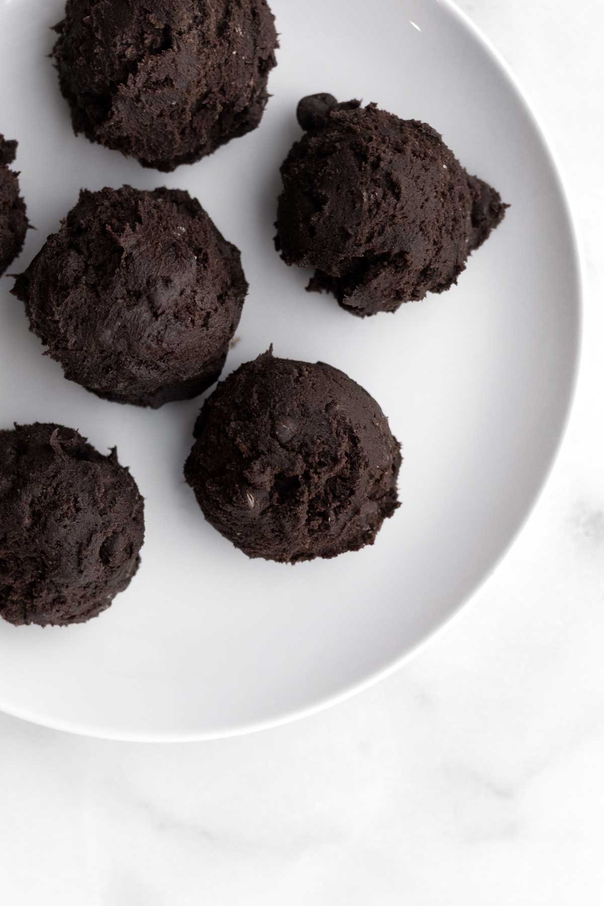 Scooped chocolate chip chocolate cookie dough on a plate.