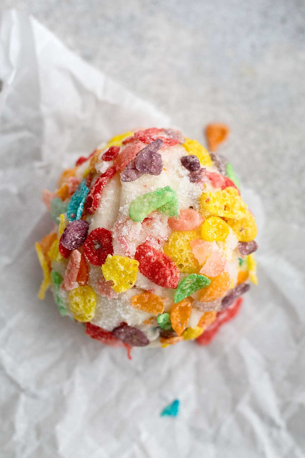 A ball of fruity pebbles cookie dough on wax paper.