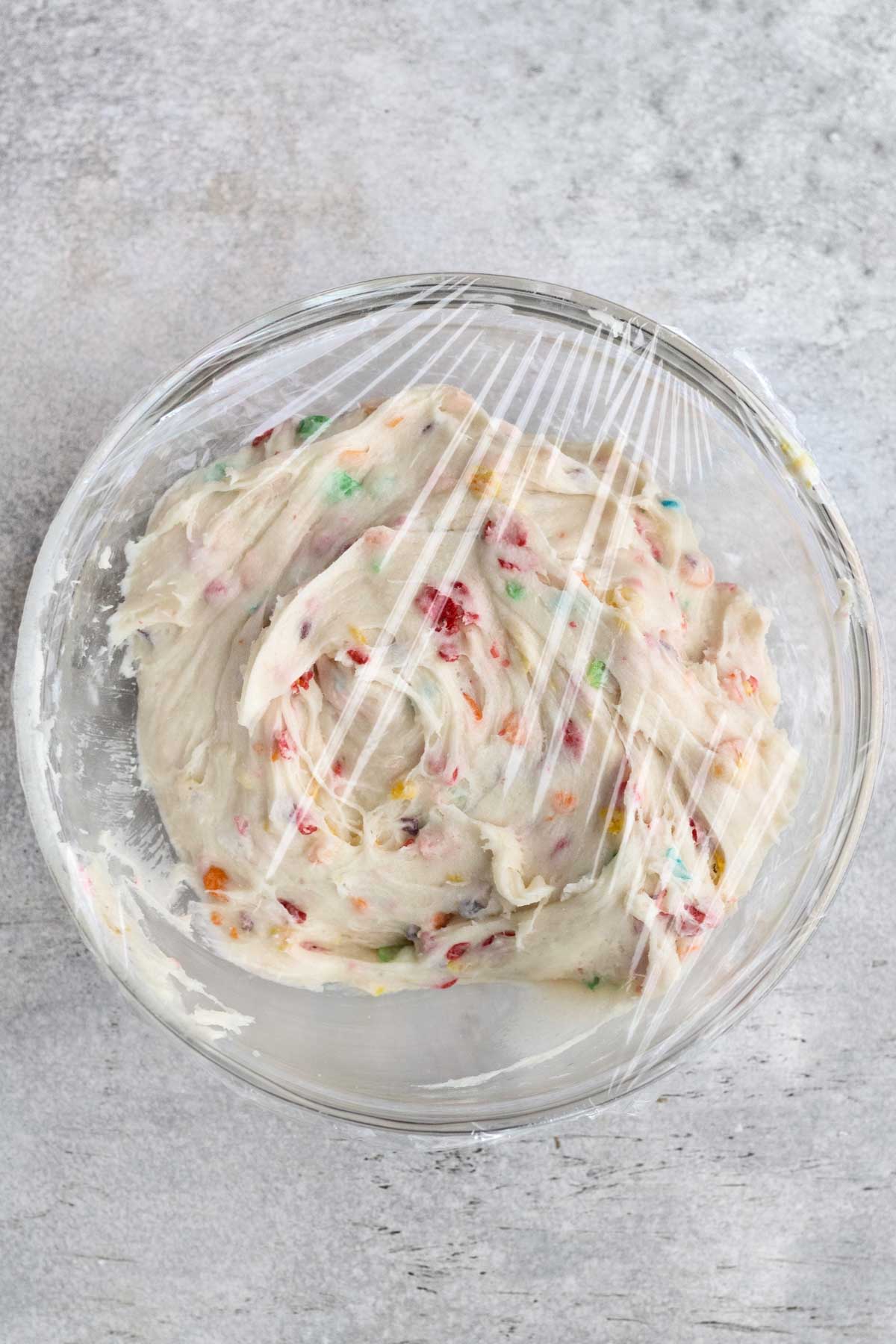 Covering the fruity pebbles cookie batter with plastic wrap in a bowl.