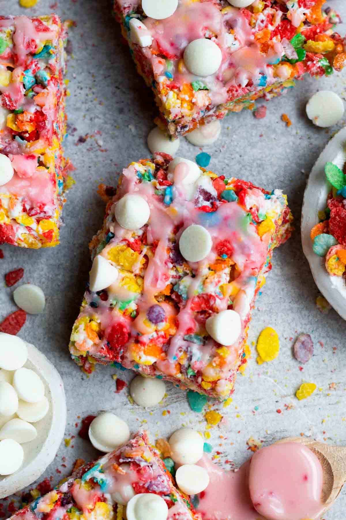 Colorful rectangular Fruity Pebble Treats topped with white chocolate chips and raspberry drizzle.