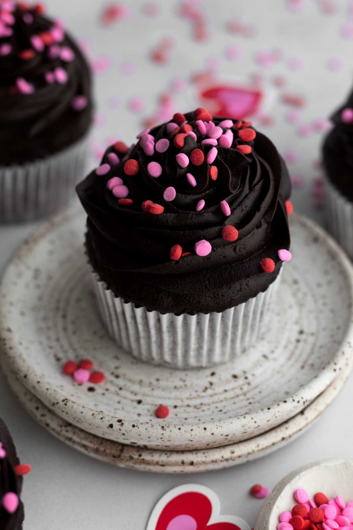 A delicious Small Batch Chocolate Cupcake with pink and red round sprinkles.