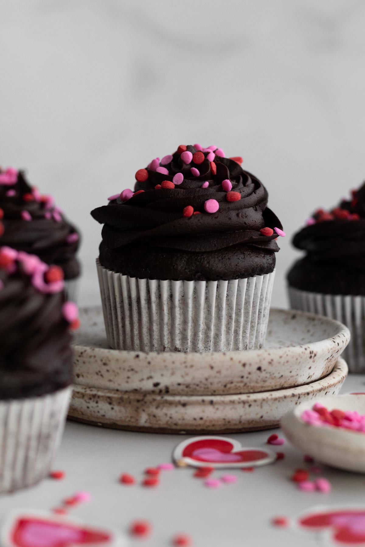 A stout chocolate cupcake sits higher than the others on ceramic plates.