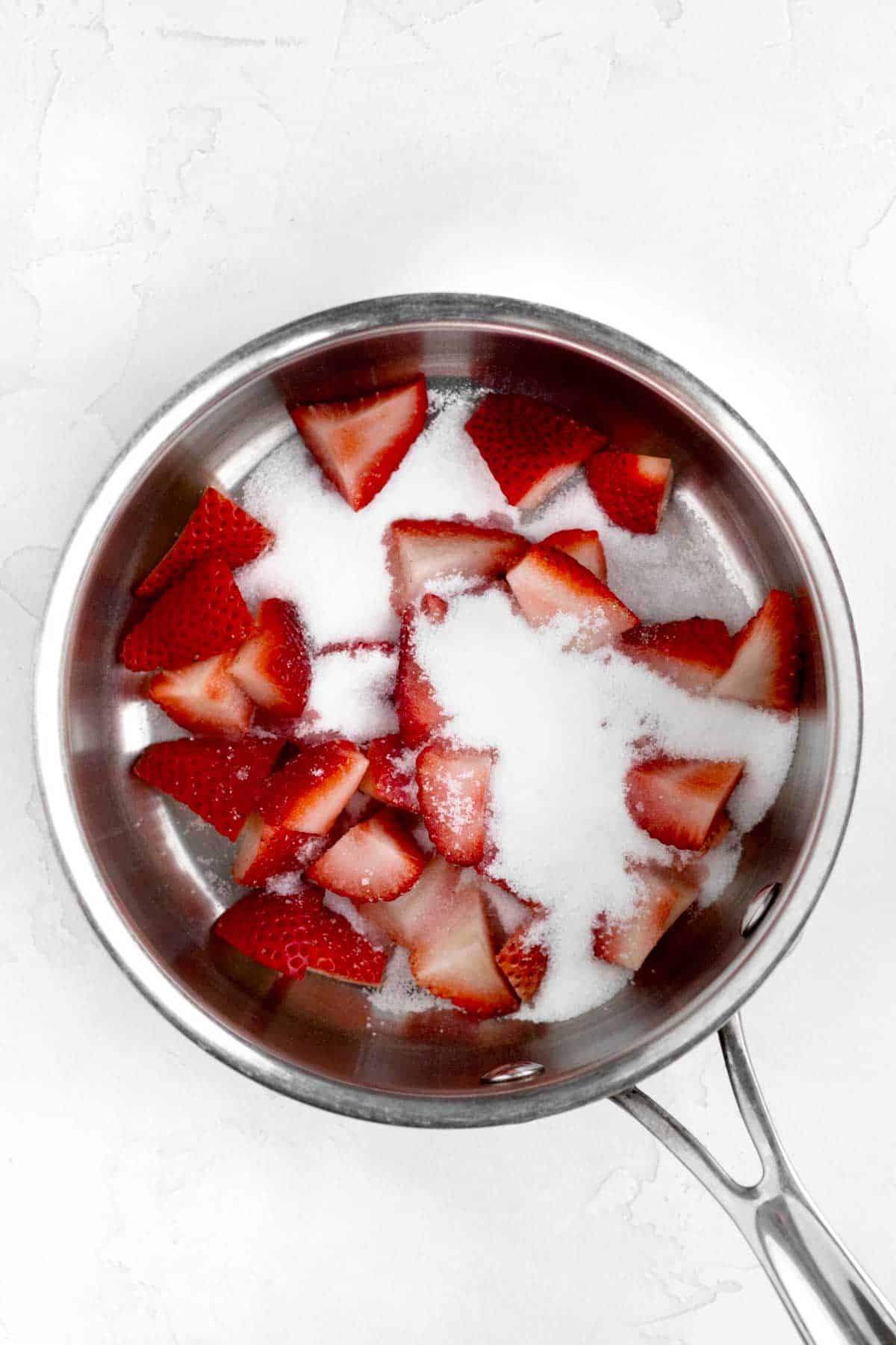 Sliced fresh strawberries and granulated sugar in a saucepan.