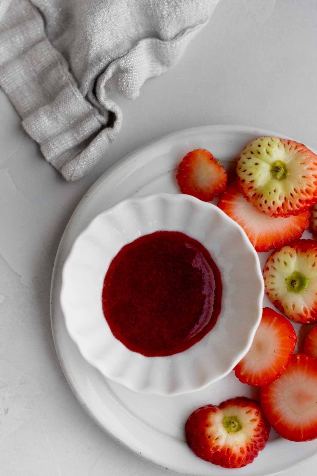 Fresh strawberry sauce in a white ramekin on a plate with strawberry tops.