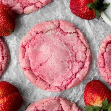 A round pink Strawberry Sugar Cookie on wax paper amongst fresh strawberries.