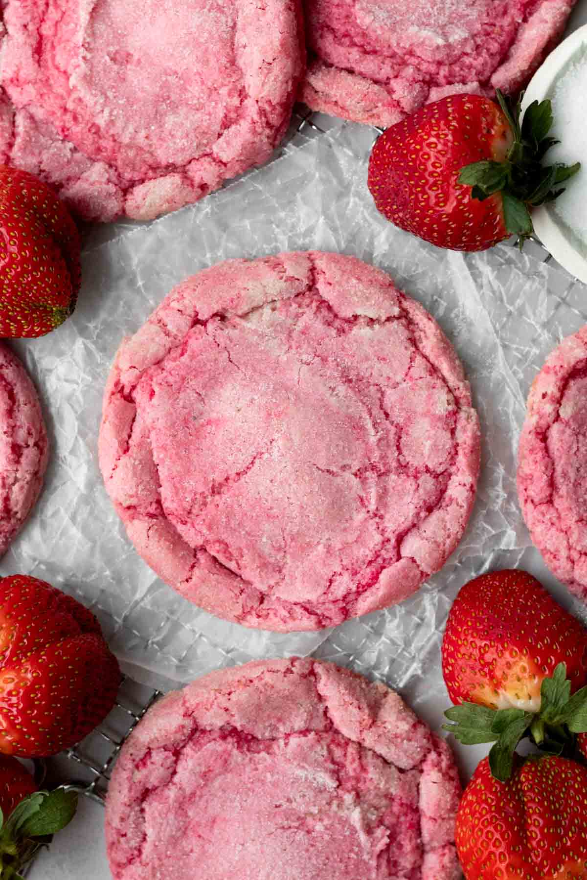 Round delicious pink Strawberry Sugar Cookie on wax paper amongst fresh strawberries.