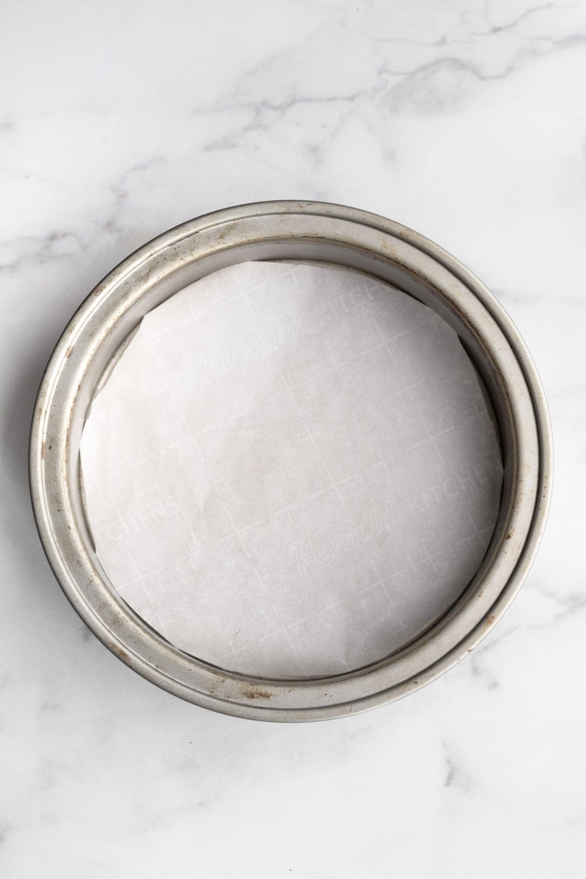 A cake pan lined with a circle of parchment paper.