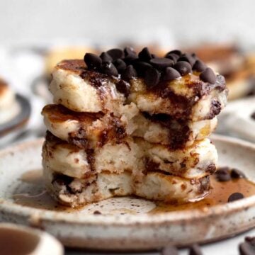 A stack of chocolate chip covered Mini Pancakes cut down inside with maple syrup running down.