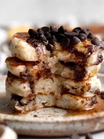 A stack of chocolate chip covered Mini Pancakes cut down inside with maple syrup running down.