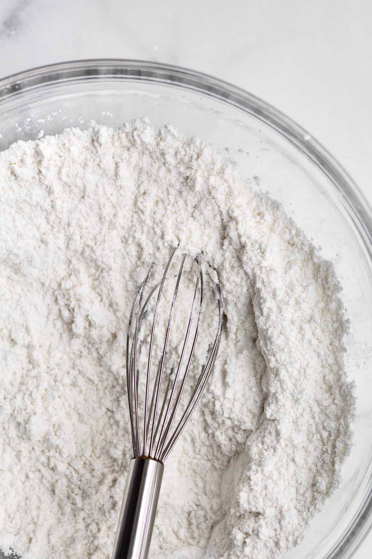 A bowl of the dry ingredients with a whisk.