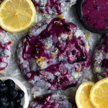 Vibrant purple Lemon Blueberry Cookies covered in sugar and lemon zest drizzled in delicious blueberry glaze.