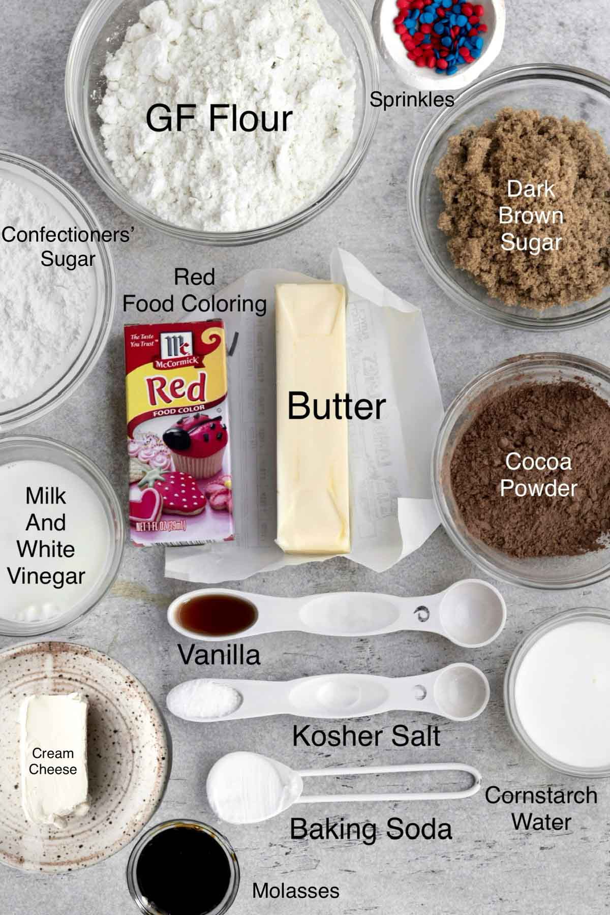 Gluten free flour, red and blue sprinkles, confectioners' sugar, red food coloring, butter, dark brown sugar, milk and white vinegar, vanilla, cocoa powder, cream cheese, kosher salt, cornstarch water, baking soda and molasses in separate containers.