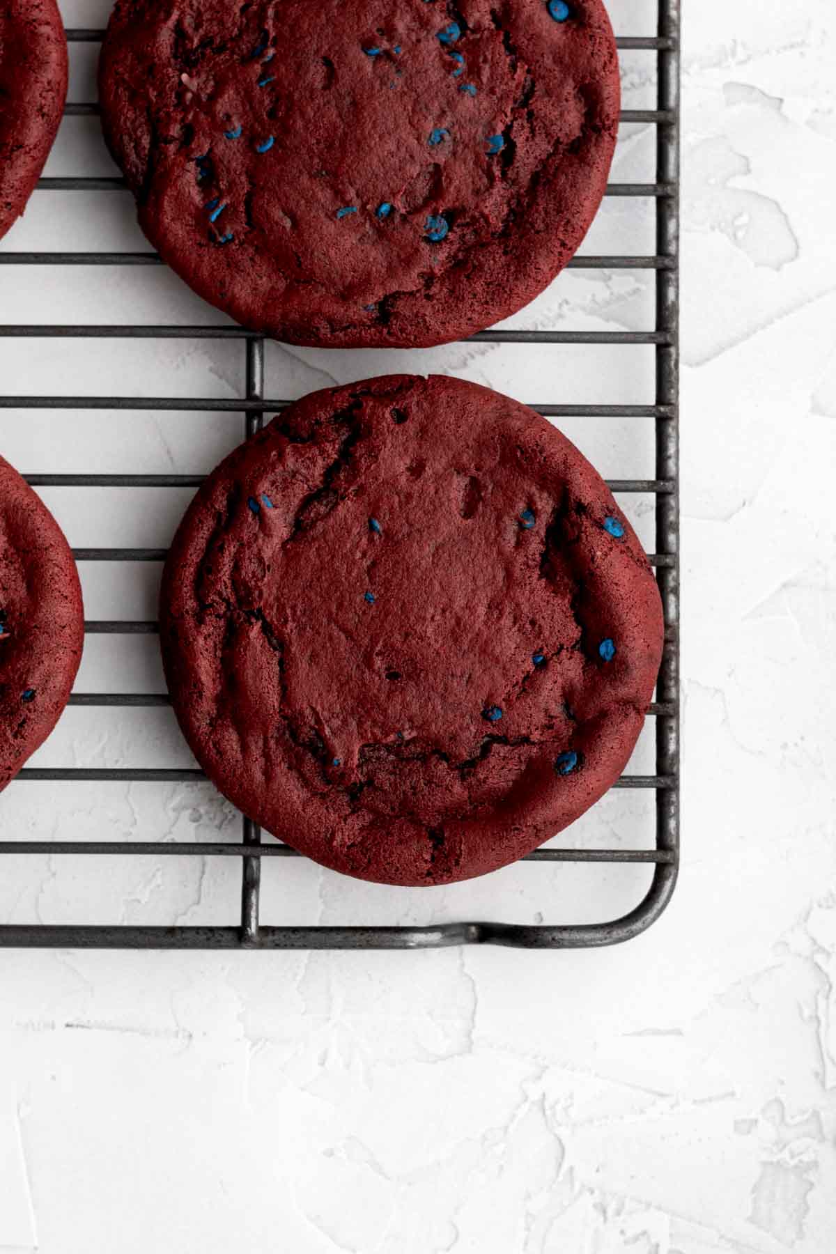 Baked and soft red cookies with blue sprinkles on a cooling rack.