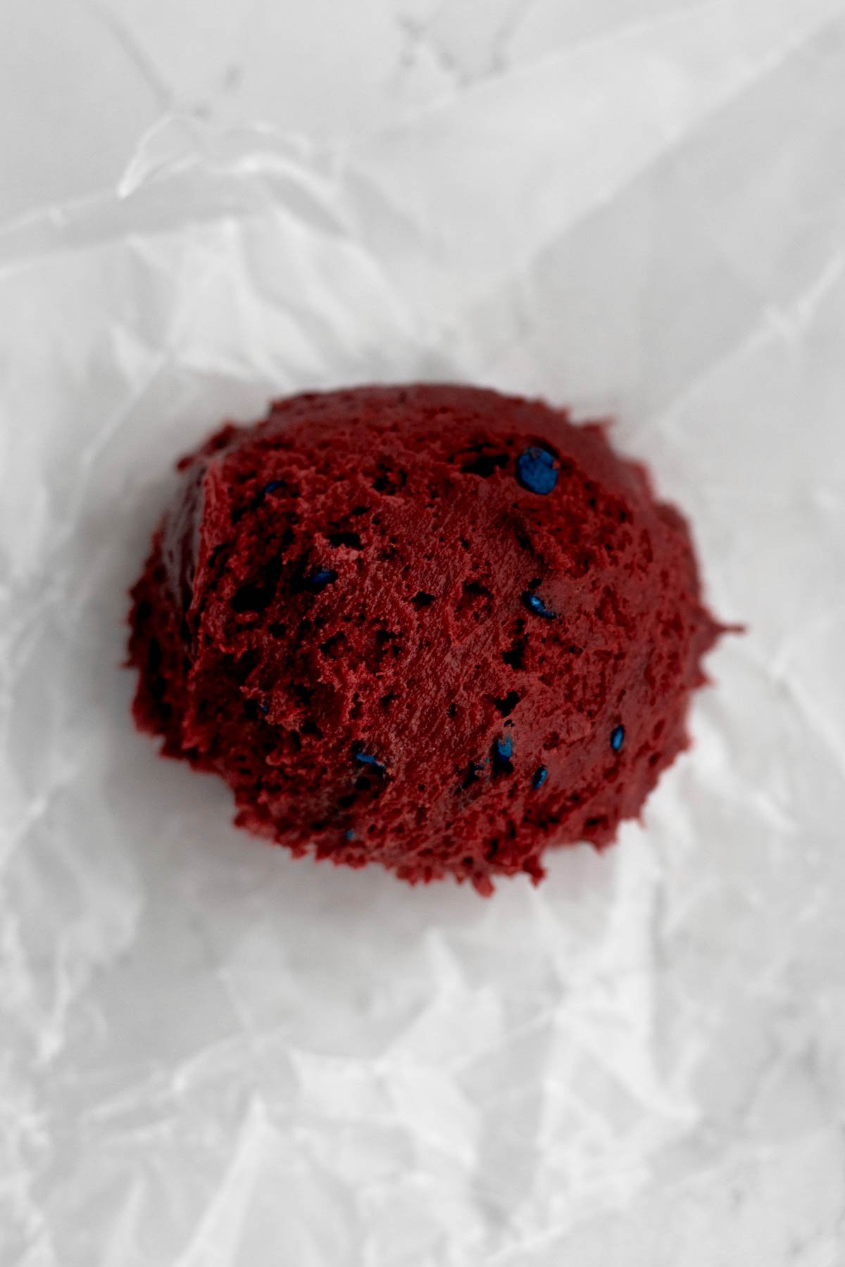 A scooped ball of red velvet cookie dough infused with blue sprinkles.
