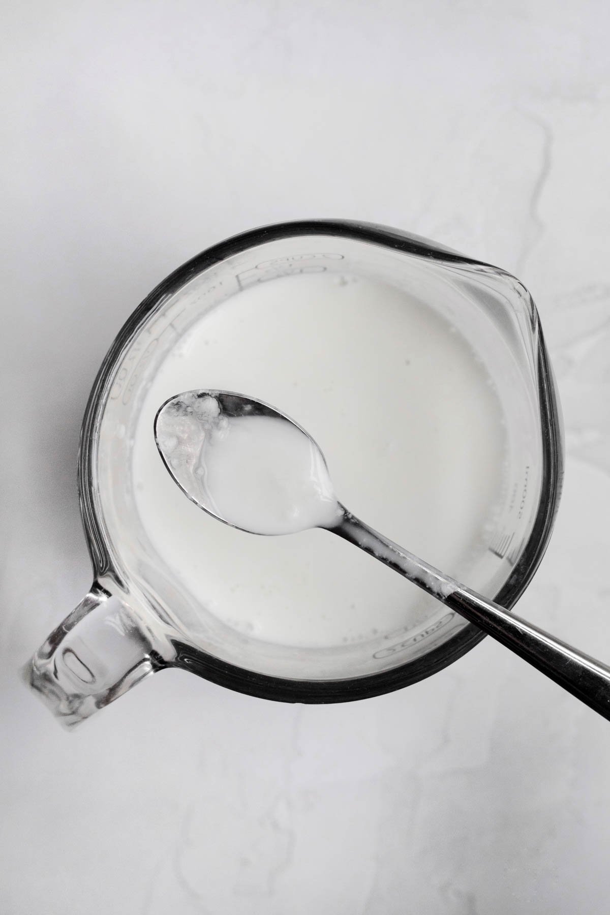 White homemade buttermilk in a measuring cup with a spoon.