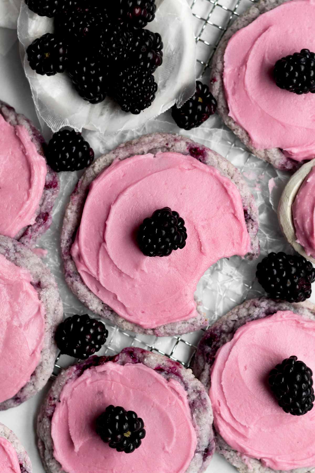 Blackberry Cookies with sweet blackberry frosting with extra fresh blackberries strewn amongst them on wax paper.