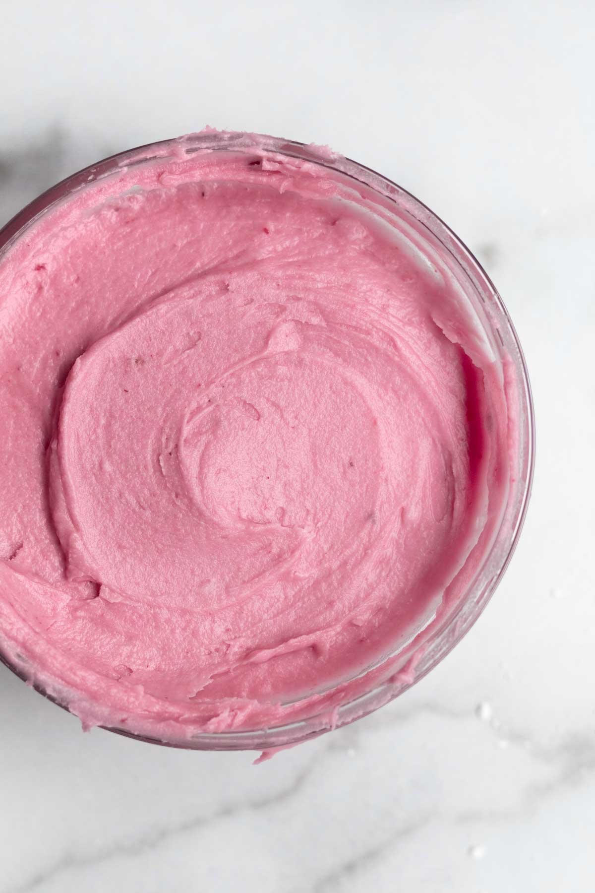 The pink and creamy blackberry frosting fills a glass bowl.