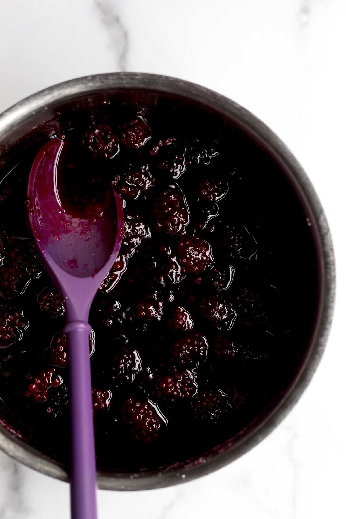 Heating up the blackberries and sugar and mixing with a purple spatula.