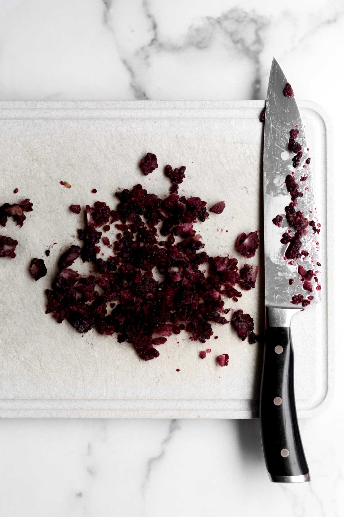 Chopped frozen blackberries on a cutting board with a knife.