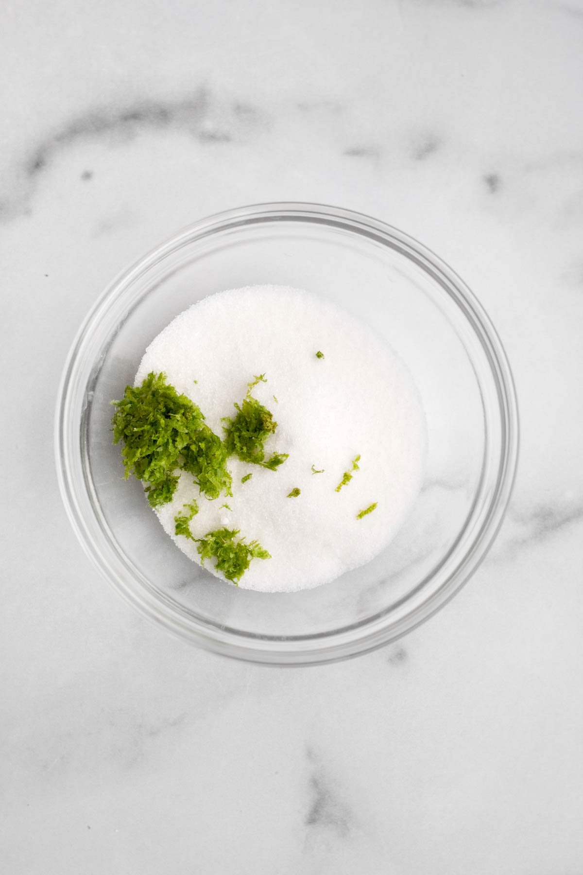 Bright green key lime zest atop a bowl of sugar.