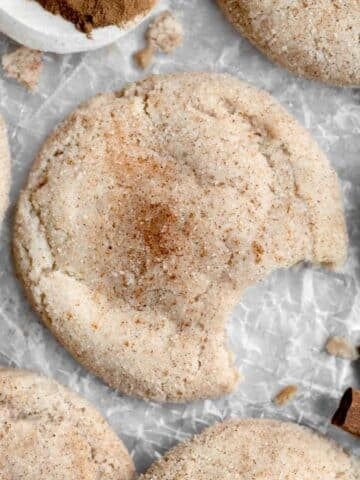 A delicious Gluten Free Snickerdoodle covered in cinnamon sugar with a bite taken out.