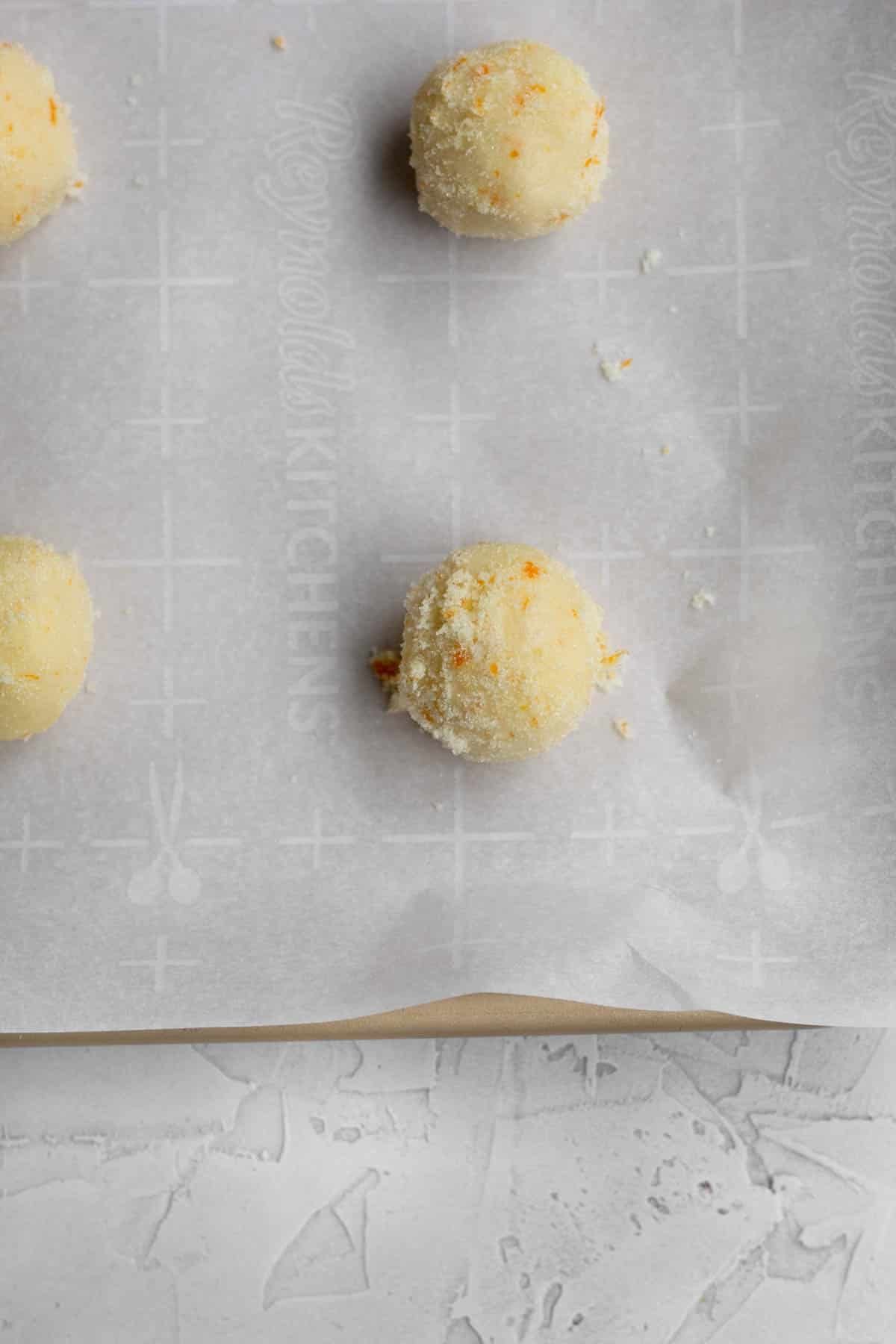 Scooped balls of Orange Shortbread Cookie dough balls on parchment paper.