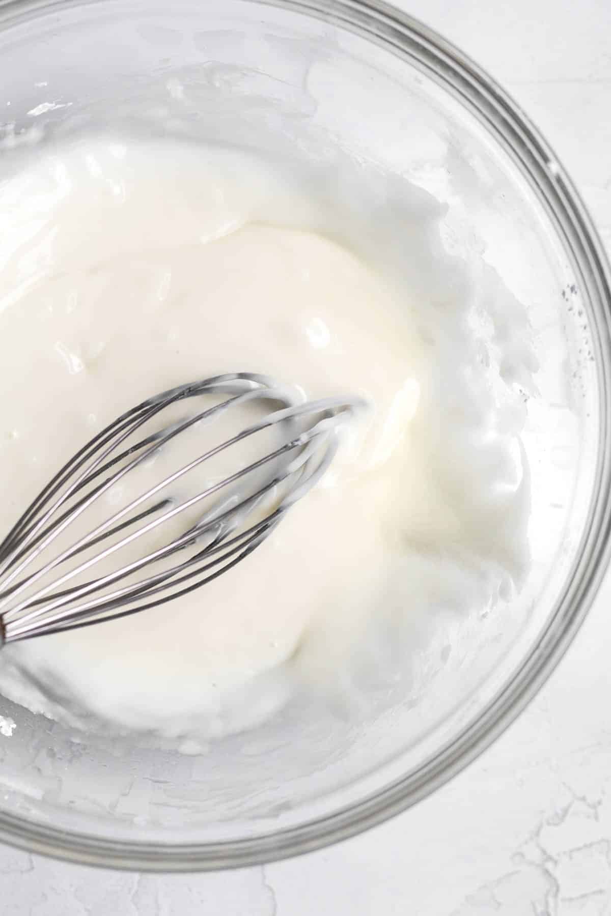 A warm sugary vanilla glaze in a glass bowl with a whisk.