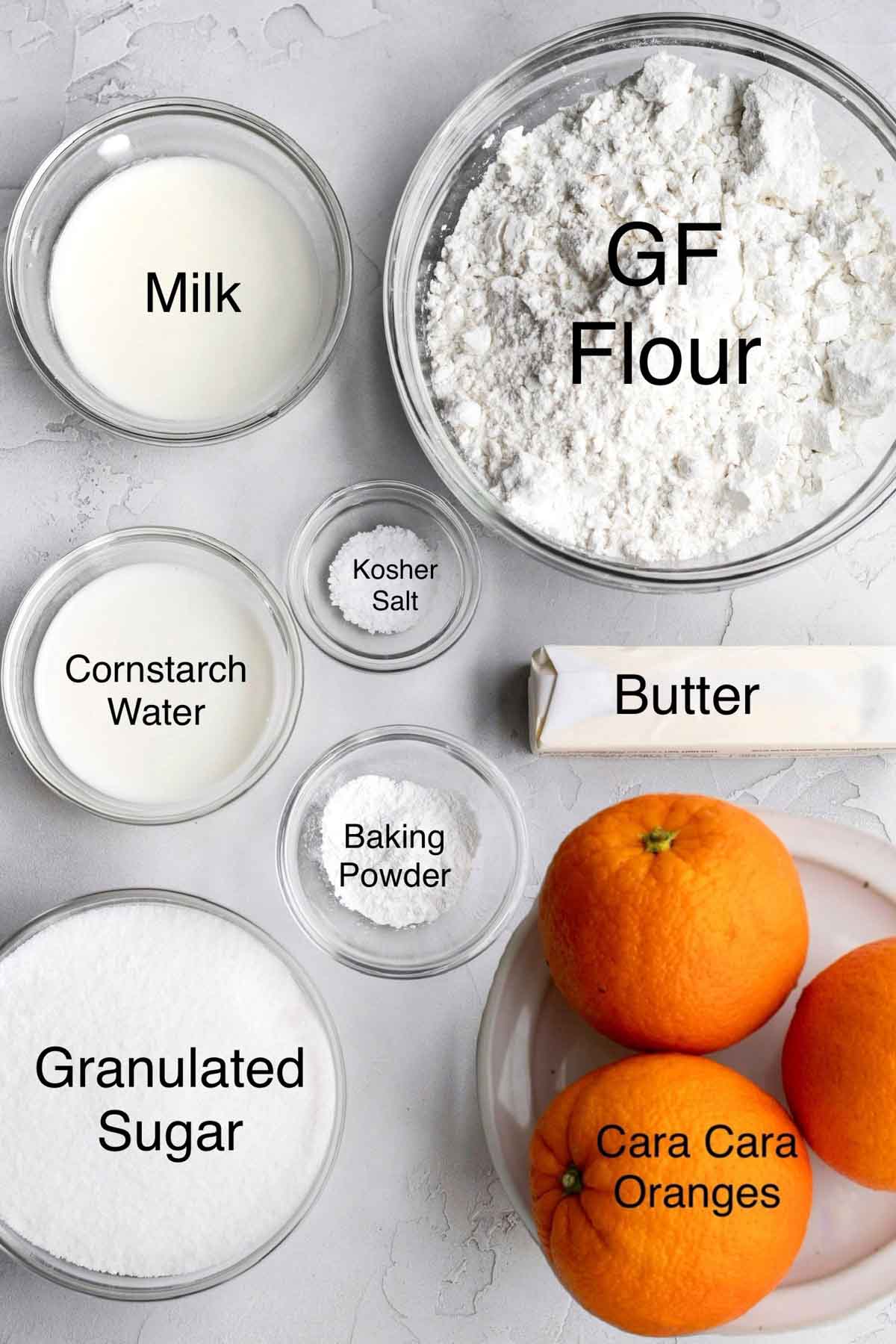 Milk, gluten free flour, cornstarch water, kosher salt, butter, baking powder, granulated sugar and three Cara Cara oranges in separate containers.