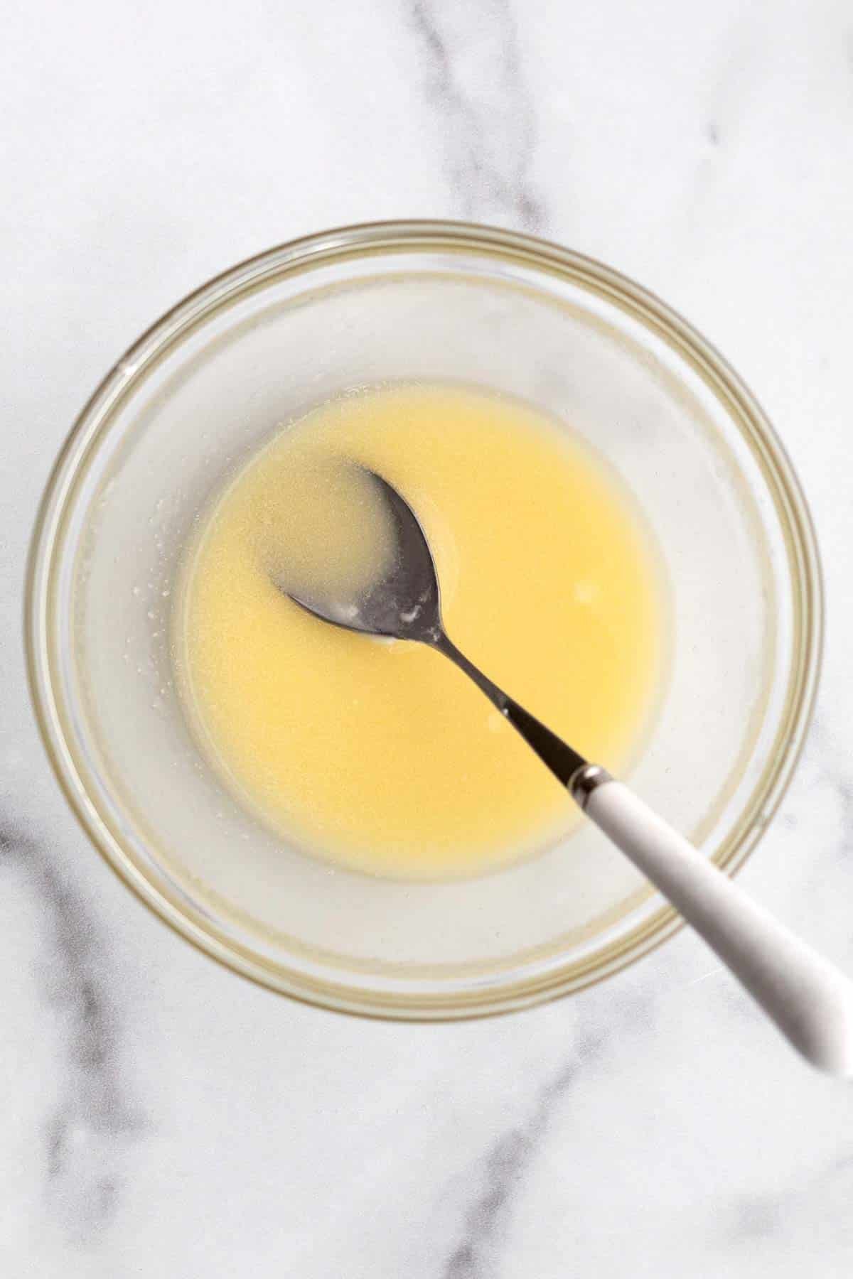 Yellow melted butter in a bowl with a spoon.