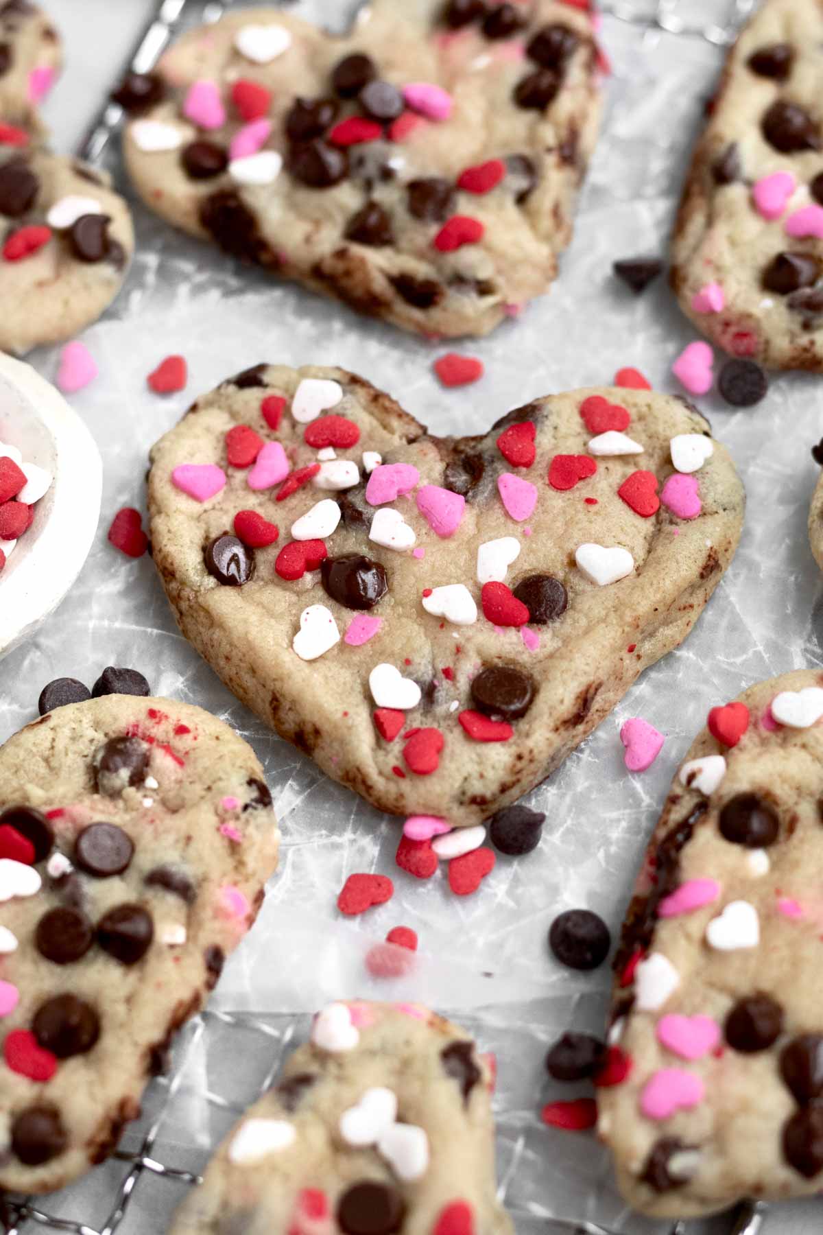 Light golden soft cookies in the shape of a heart with chocolate chips and heart sprinkles.