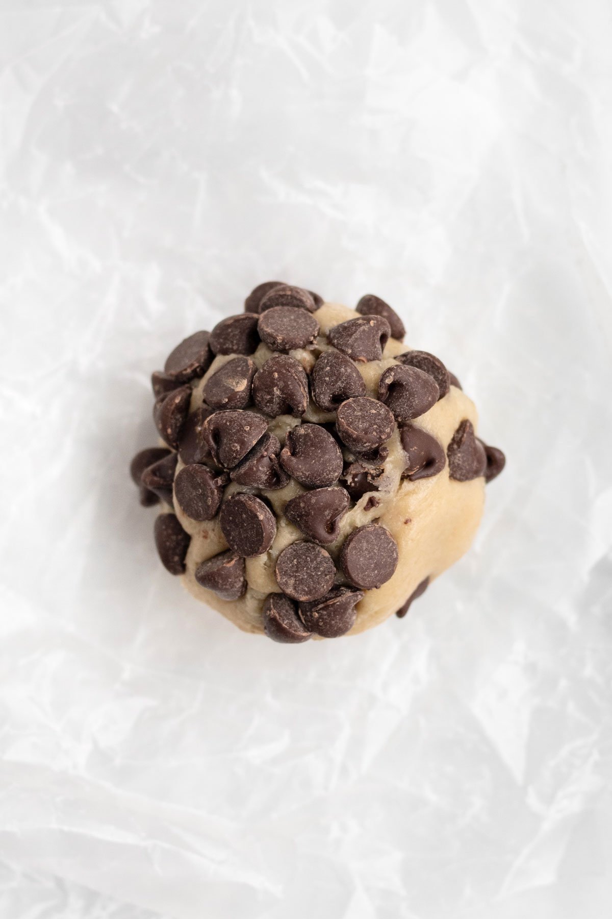 Pressing extra chocolate chips to the top of the cookie dough ball.