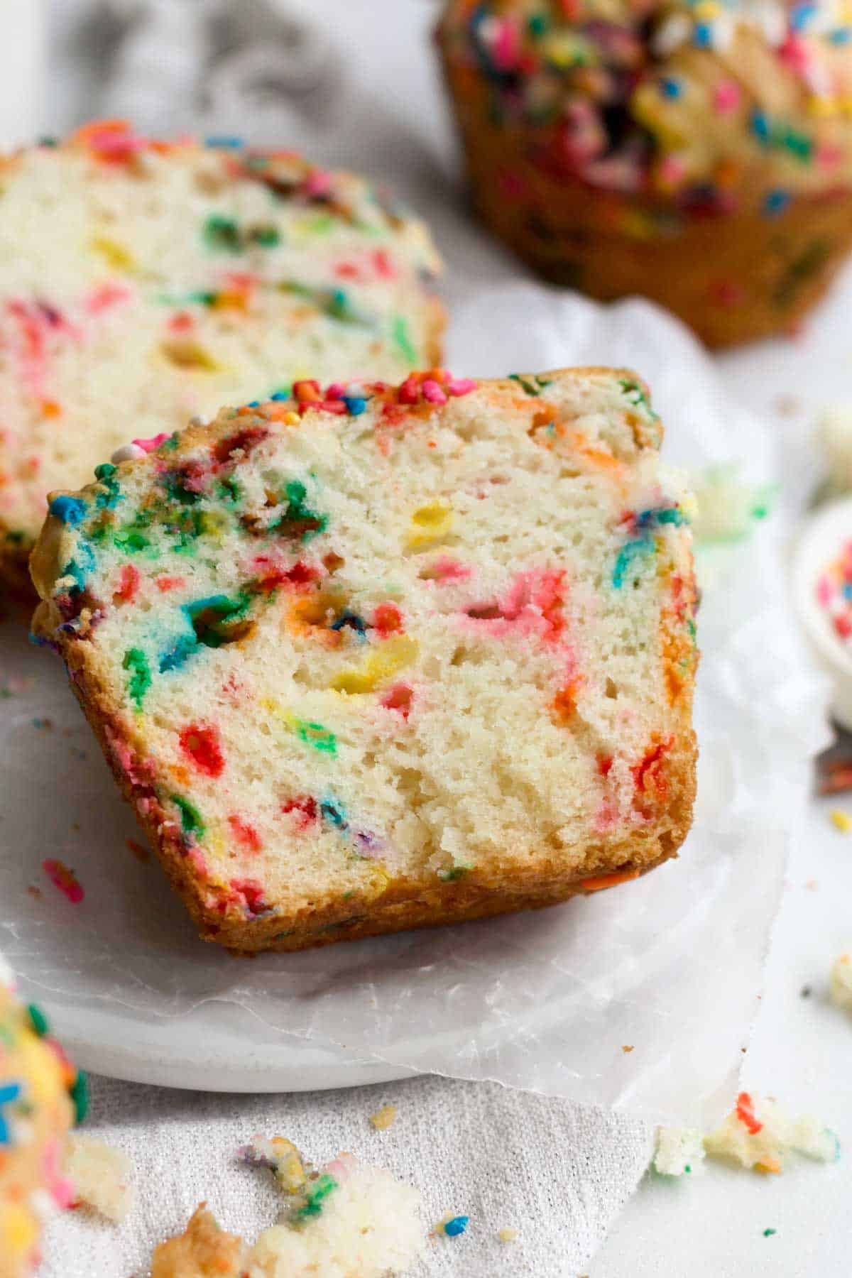 A sliced Birthday Muffin reveals its light and airy vanilla flavored interior stained by rainbow sprinkles.