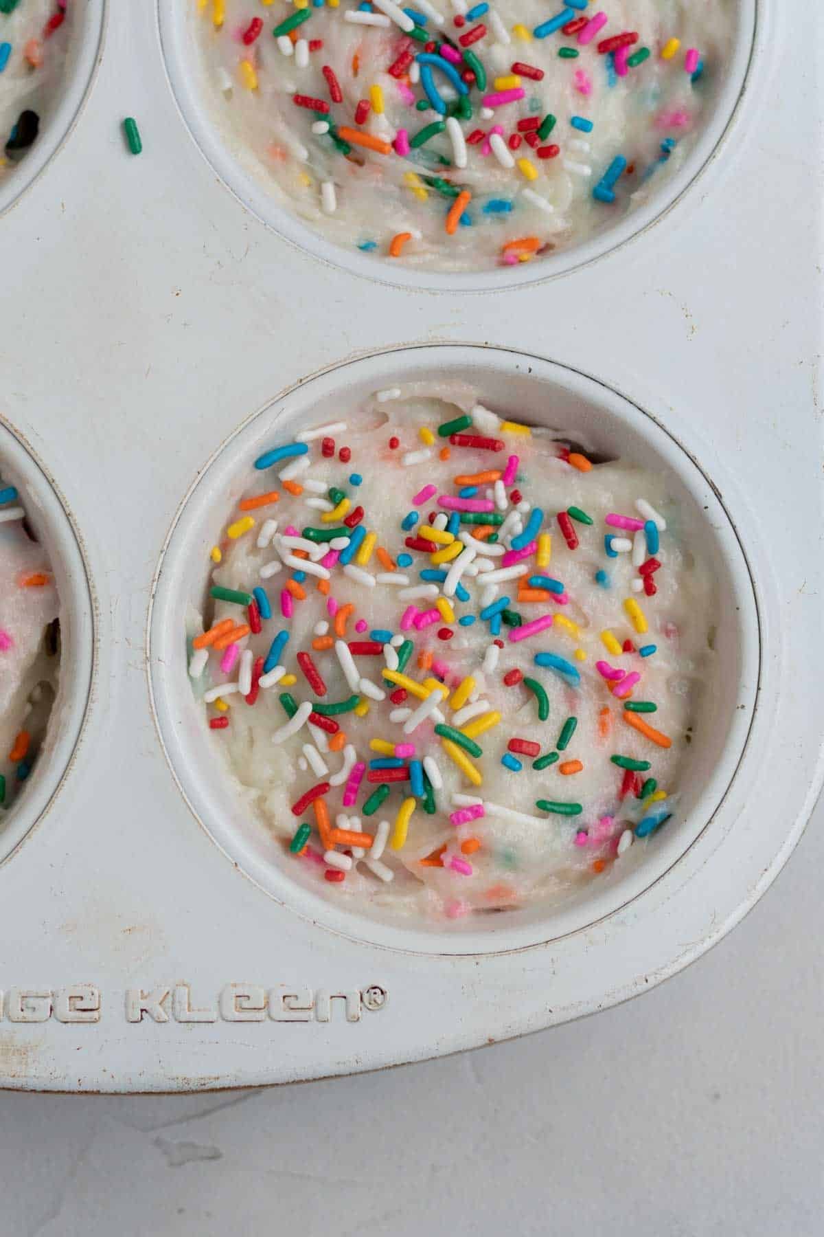 Adding extra rainbow sprinkles to the tops of the muffin batter.
