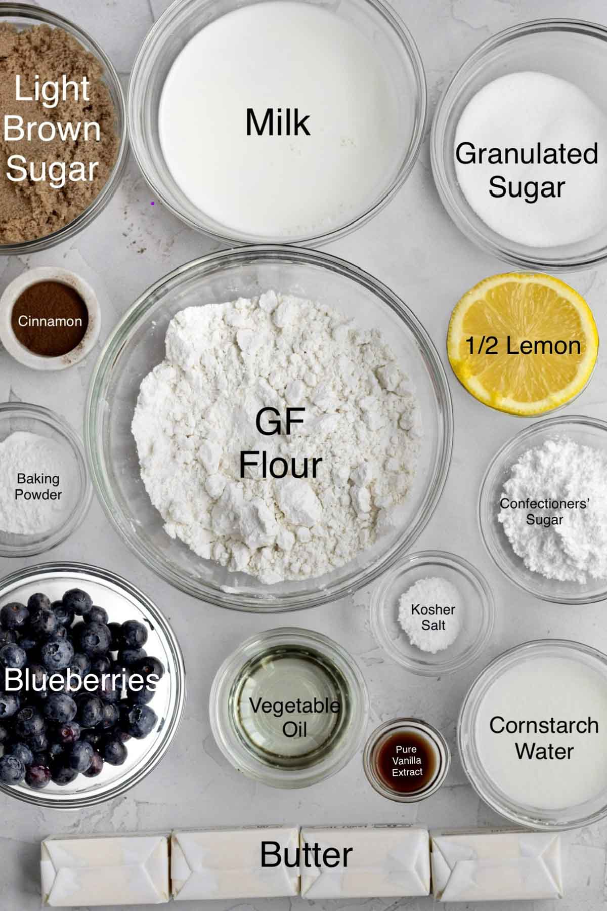 Light brown sugar, milk, granulated sugar, cinnamon, half a lemon, baking powder, gluten free flour, confectioners' sugar, blueberries, vegetable oil, kosher salt, pure vanilla extract, cornstarch water and butter in separate containers.