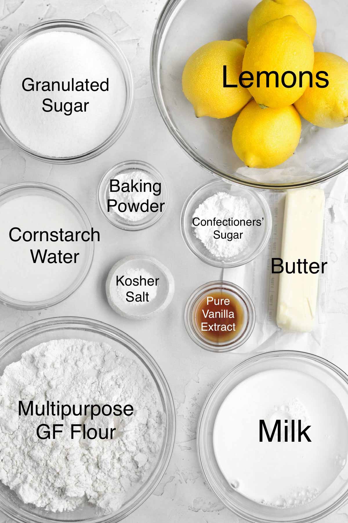 Granulated sugar, lemons, cornstarch water, baking powder, confectioners' sugar, butter, kosher salt, pure vanilla extract, multipurpose gluten free flour, and milk in separate containers.