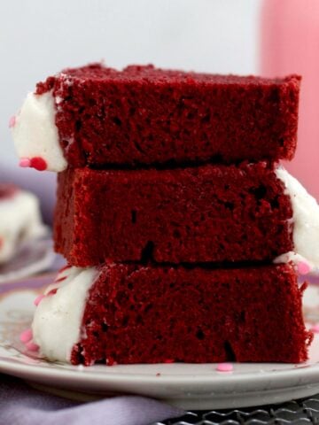 Stacked slices of Red Velvet Loaf Cake with frosting and sprinkles showcasing its vibrant texture.