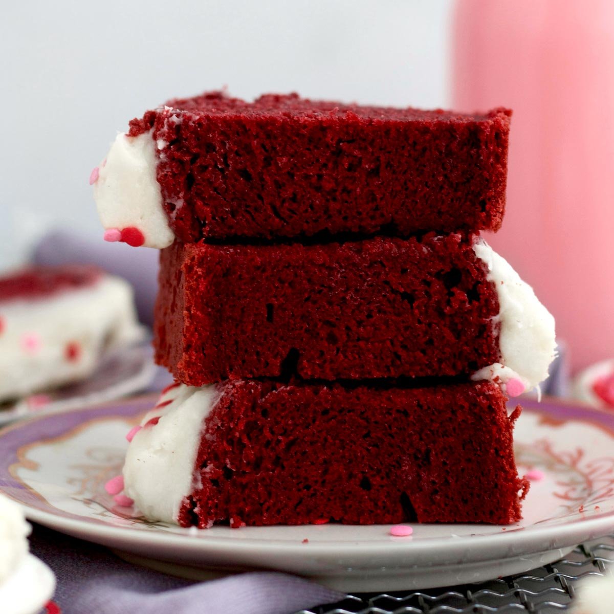 Stacked slices of Red Velvet Loaf Cake with frosting and sprinkles showcasing its vibrant texture.