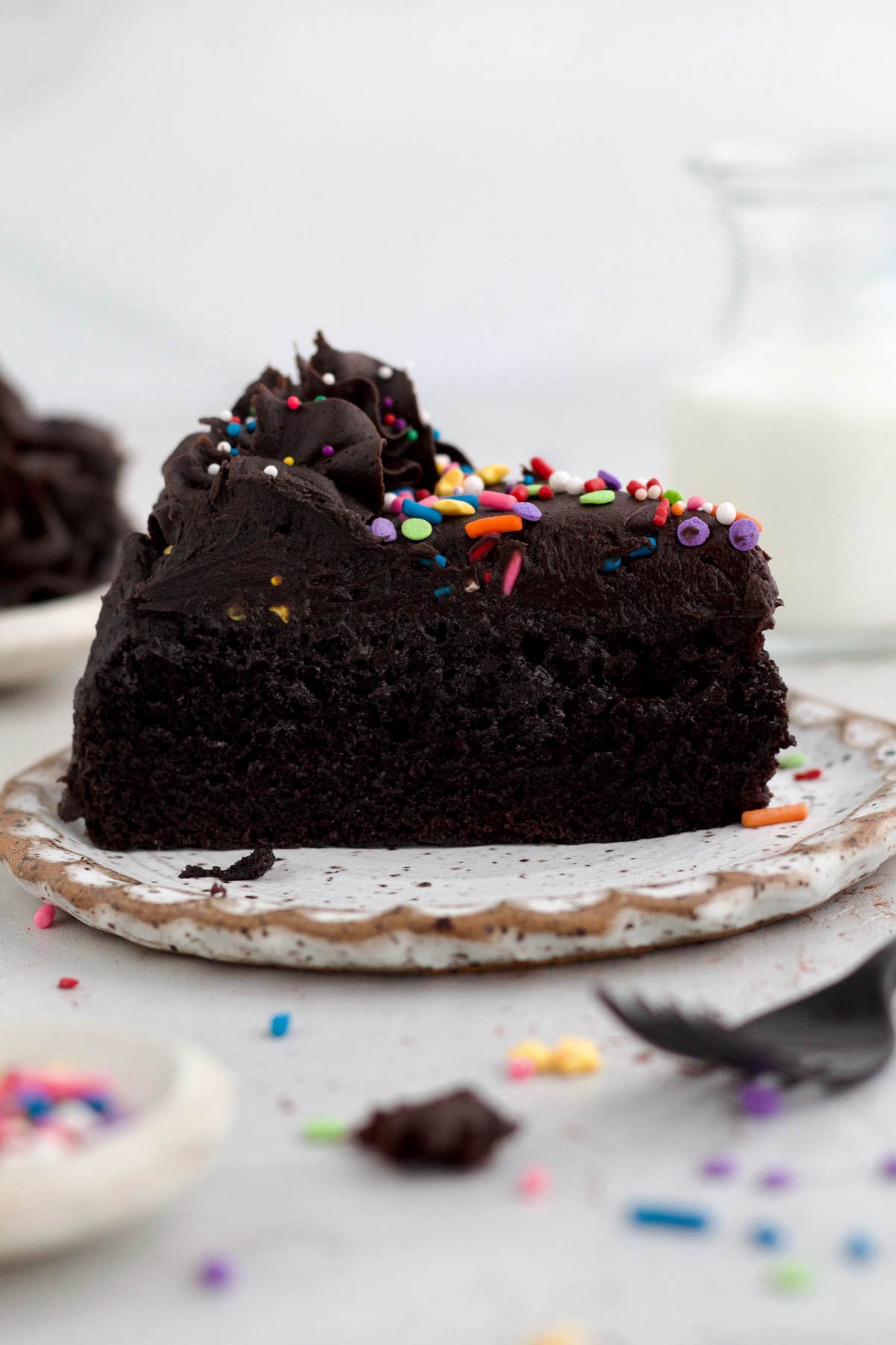 An indulgent Slice of rich, dark chocolate cake with cream cheese frosting and colorful sprinkles.