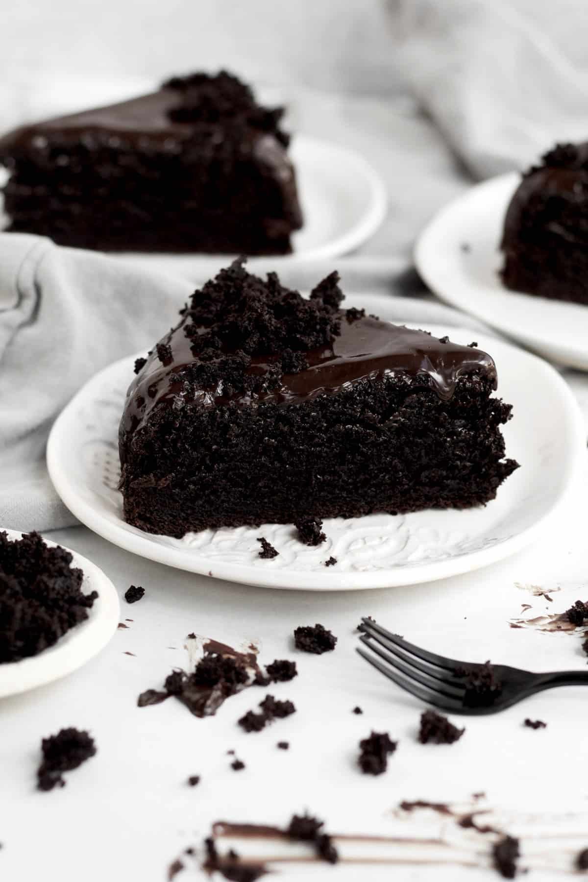 Crumbled cake sits atop a generous slice of Chocolate Ganache Cake on a ceramic plate.