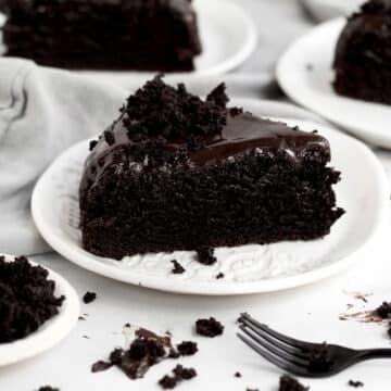 Crumbled cake sits atop a generous slice of Chocolate Ganache Cake on a ceramic plate.