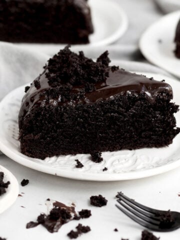 Crumbled cake sits atop a generous slice of Chocolate Ganache Cake on a ceramic plate.