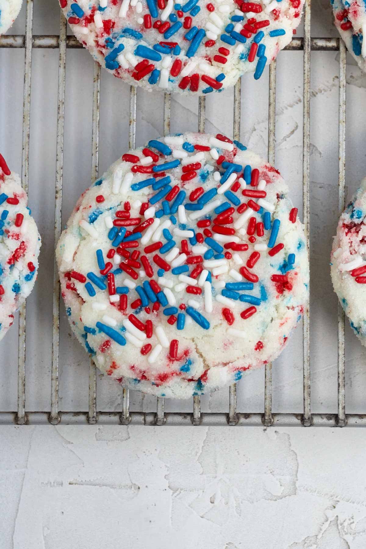Red, white and blue sprinkled crispy 4th of July Sugar Cookies resting on a baking rack.