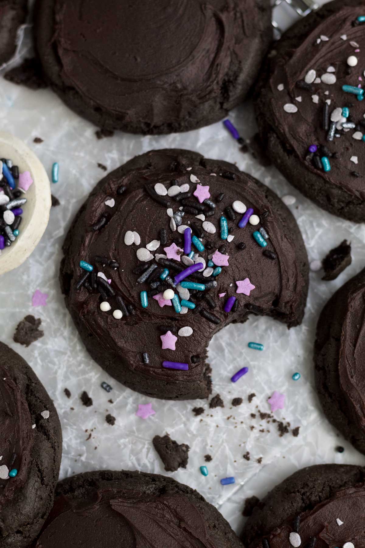 A delicious and decadent Frosted Chocolate Cookie with purple space sprinkles missing a bite.