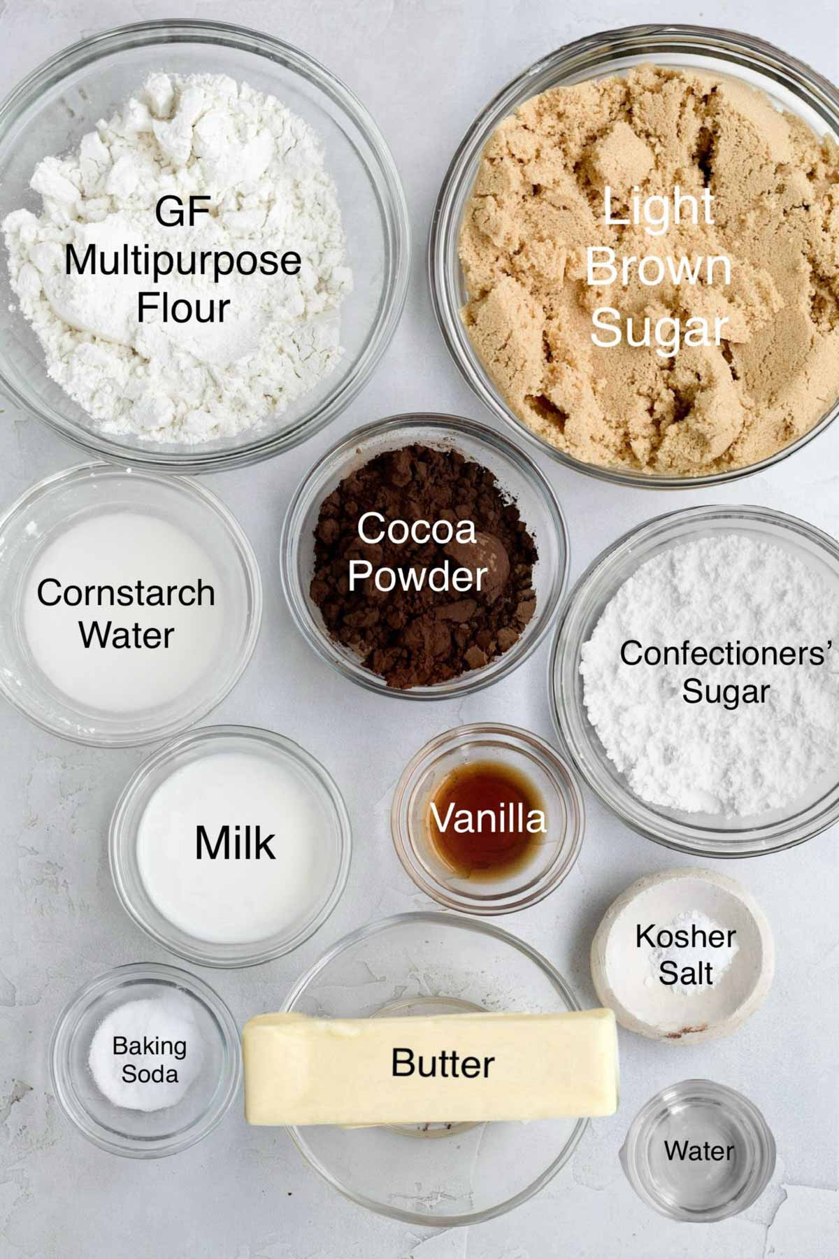Bowls of gluten free multipurpose flour, light brown sugar, cornstarch water, cocoa powder, confectioners' sugar, milk, vanilla kosher salt, baking soda, butter and water.