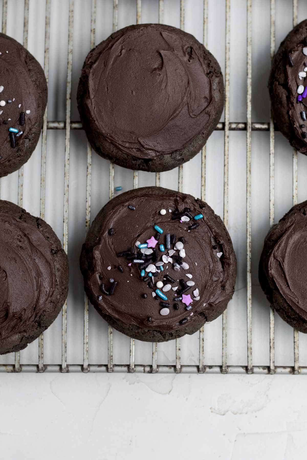 Frosting the tops of chocolate cookies with chocolate frosting and adding sprinkles.