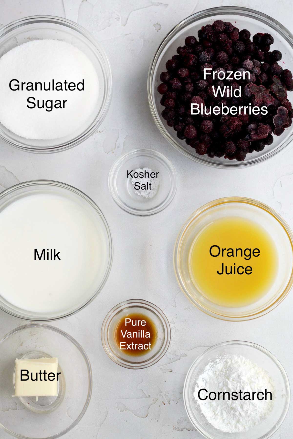Bowls of granulate sugar, frozen wild blueberries, kosher salt, milk, orange juice, pure vanilla extract, butter and cornstarch.