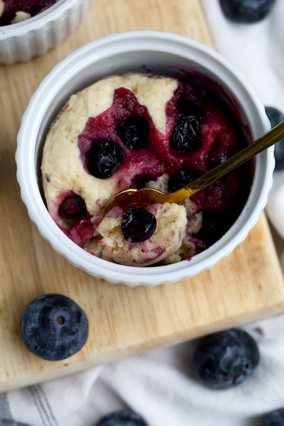 A dainty golden spoon picks up some light and fluffy blueberry mug cake.