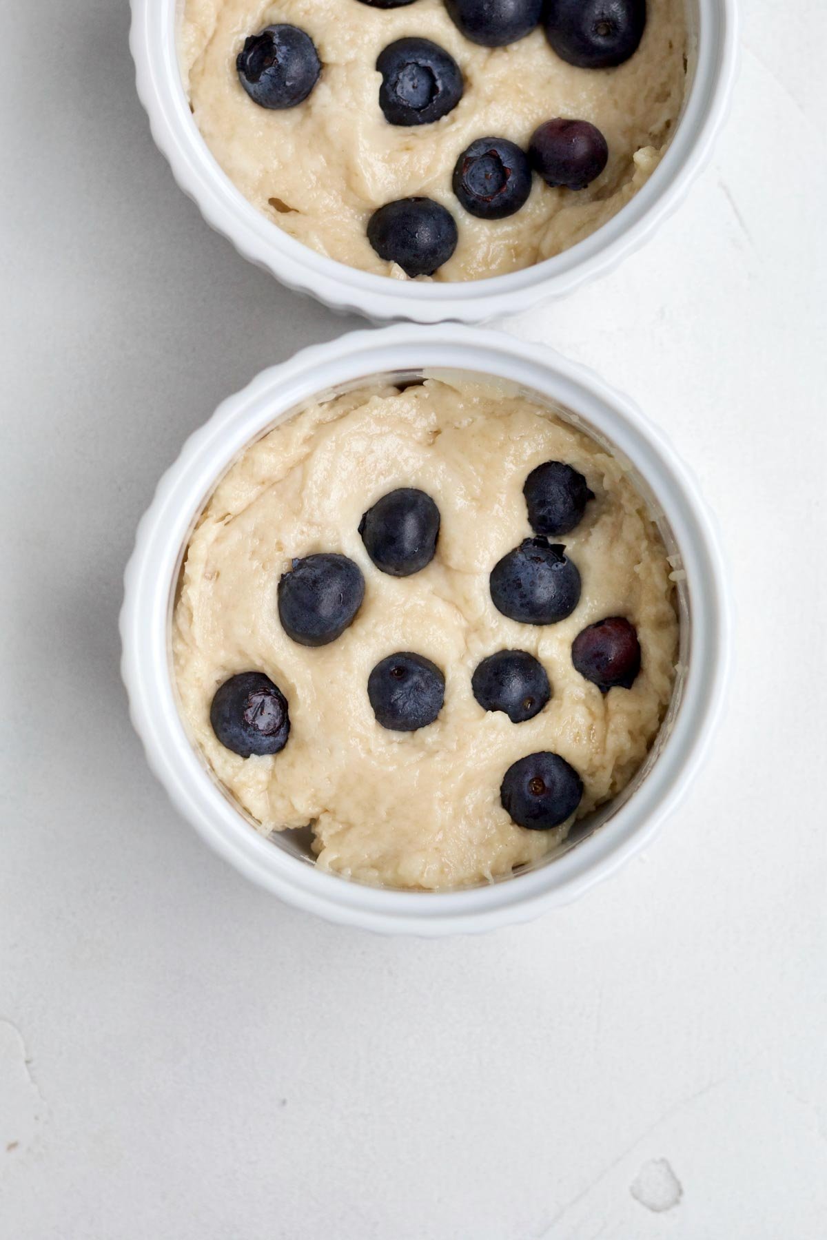 Filling ramekins with batter and pressing fresh blueberries to the top.