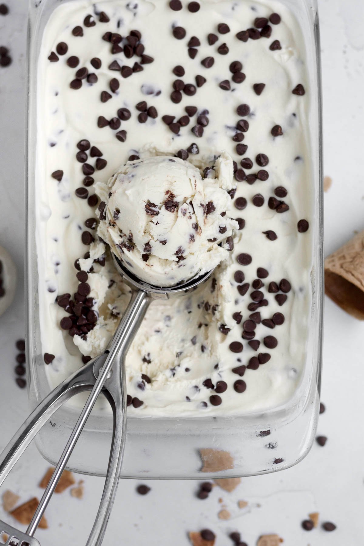 Scooping up some frozen Chocolate Chip Ice Cream from a glass container.